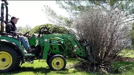 Image of a landscape contractor on a John Deere tractor removing an unwanted bush